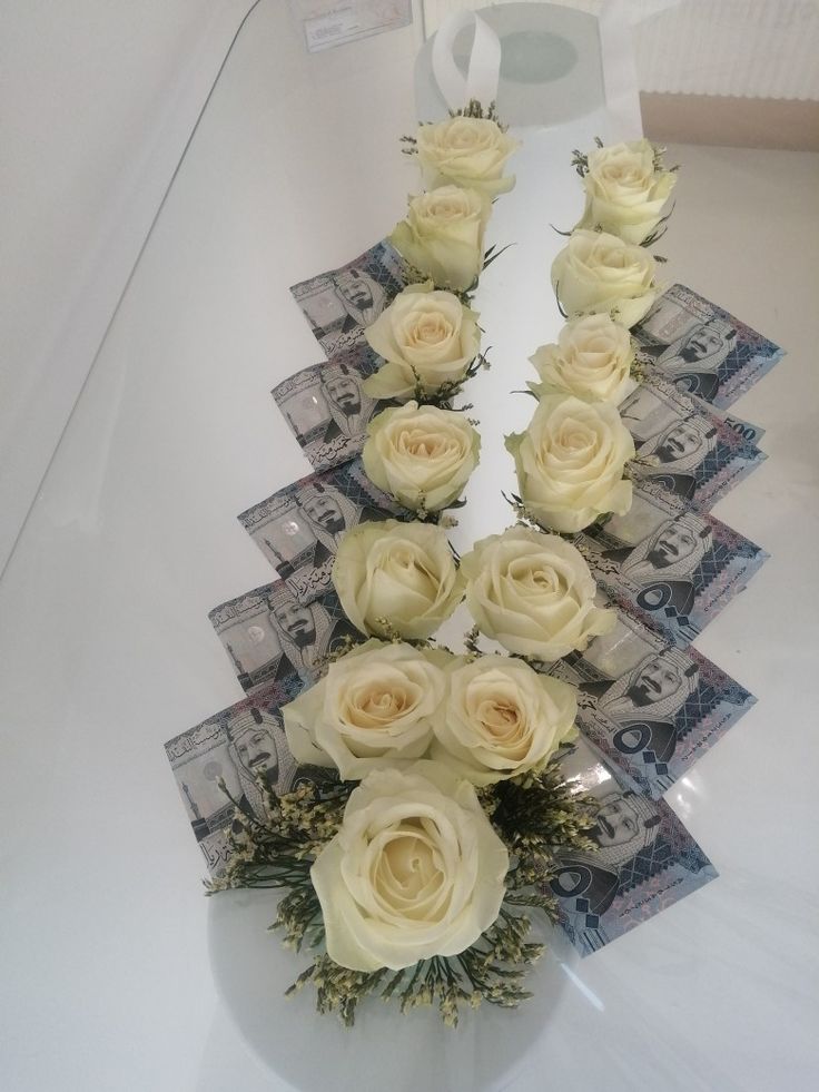 white roses are arranged in the shape of an arrow on top of money bills and flowers