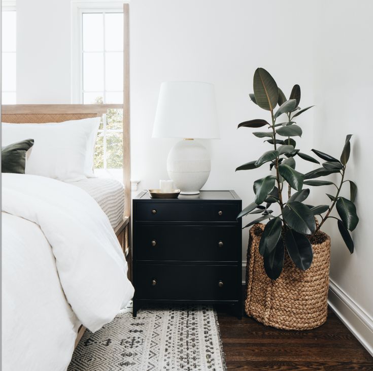 a bedroom with a bed, nightstand and potted plant on the floor next to it