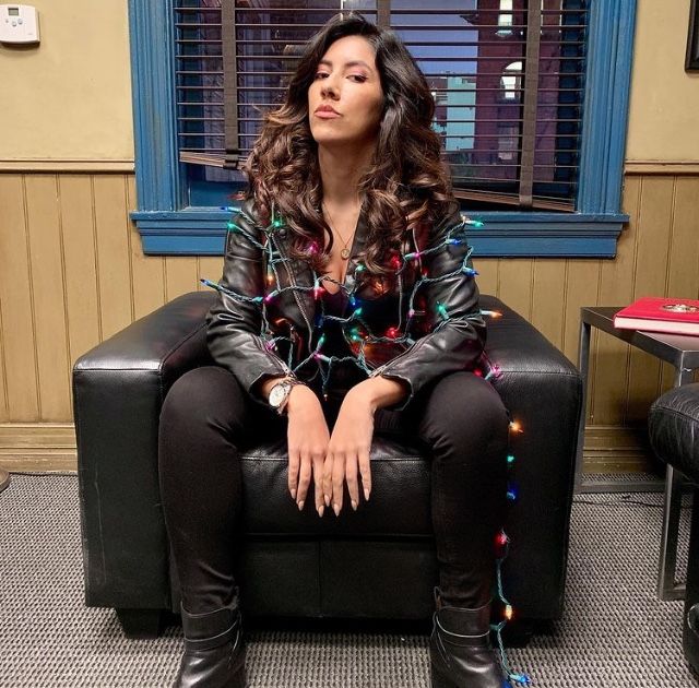 a woman sitting on top of a black couch in front of a window covered in christmas lights