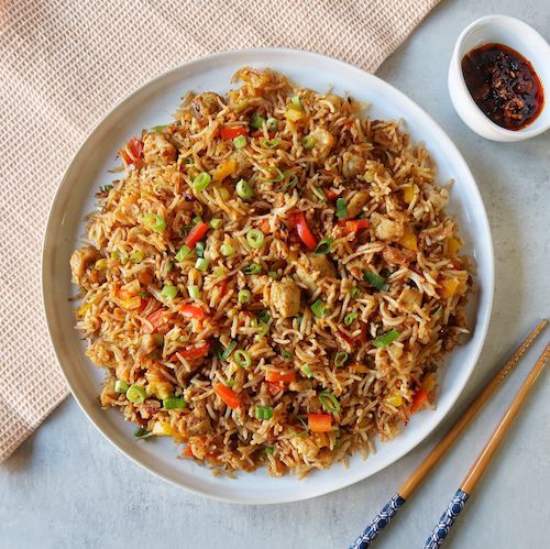 a white plate topped with fried rice next to chopsticks