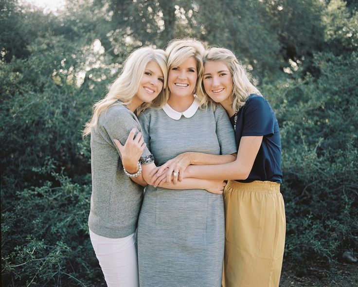 three women hugging each other in front of trees