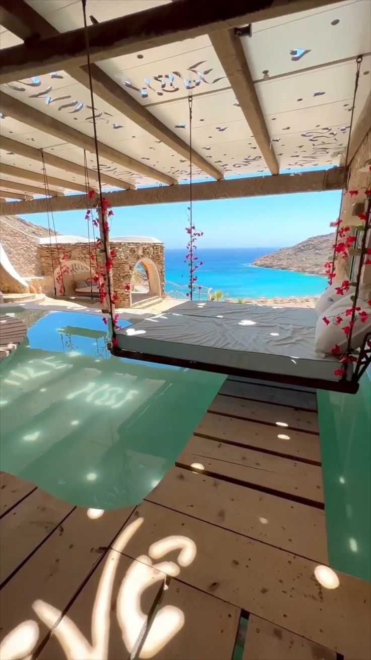 a glass table sitting on top of a wooden deck next to the ocean and water