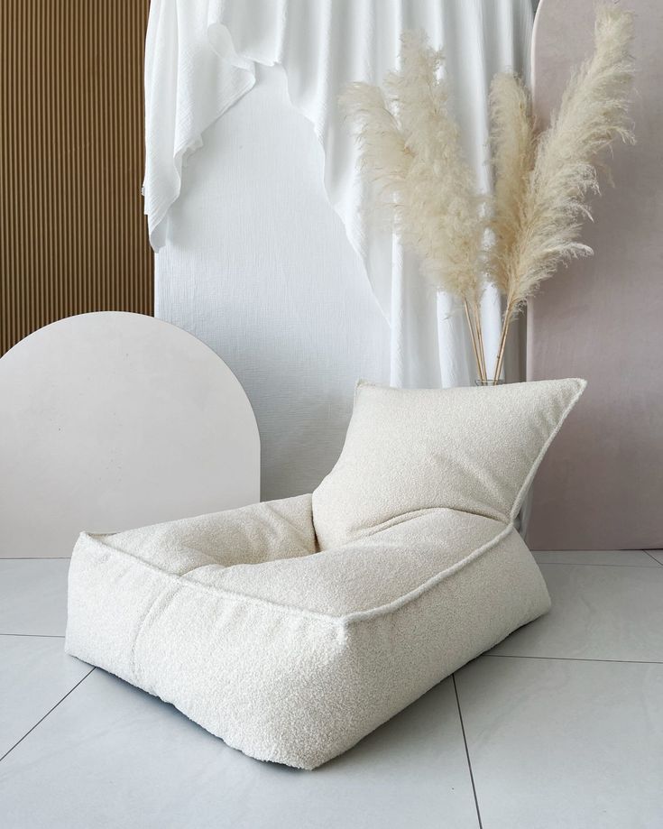 a white chair sitting on top of a tile floor next to a vase filled with dry grass