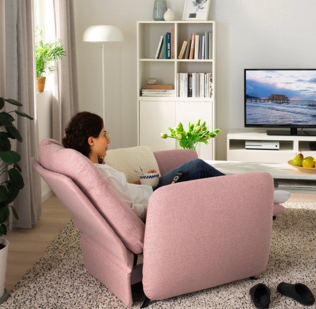 a woman sitting in a pink recliner watching tv