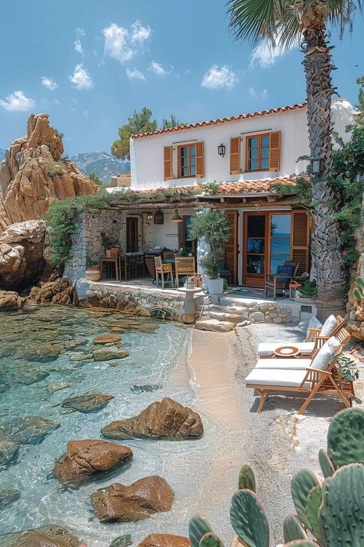 a house on the beach next to some rocks and water with chairs in front of it