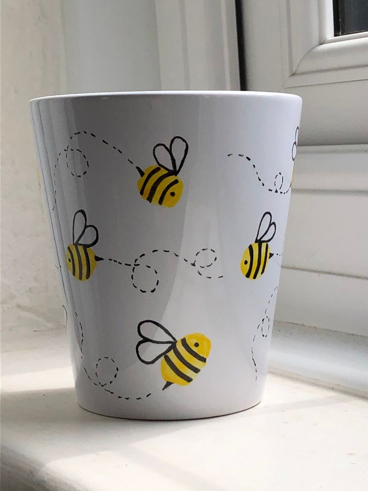 a white cup with yellow and black bees on it sitting on a window sill