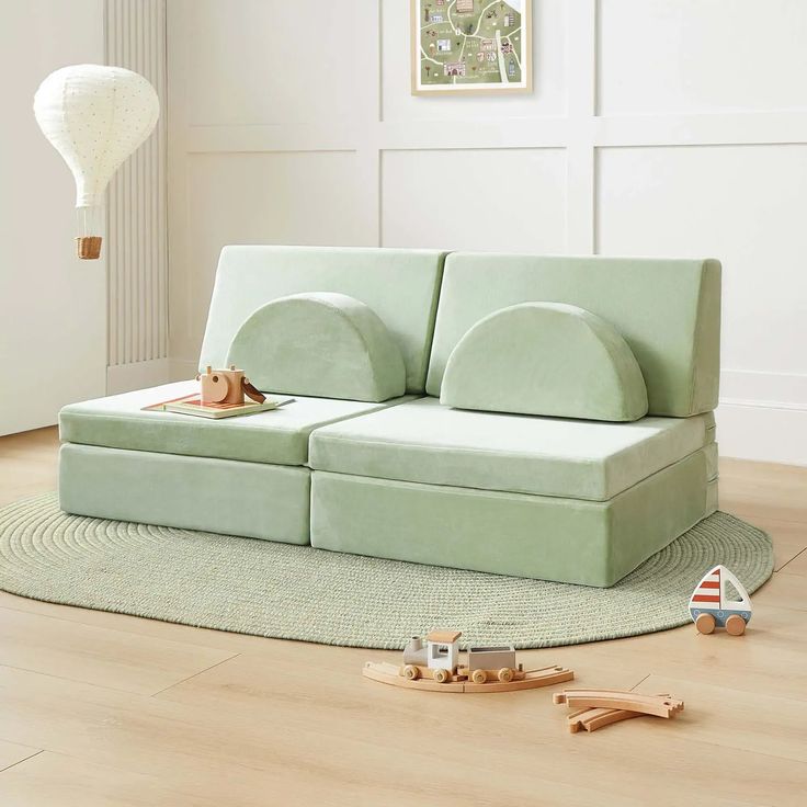 a green couch sitting on top of a wooden floor next to a toy train set