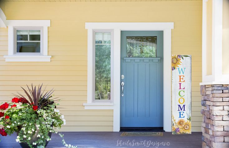 a blue front door on a yellow house with two potted plants in the foreground