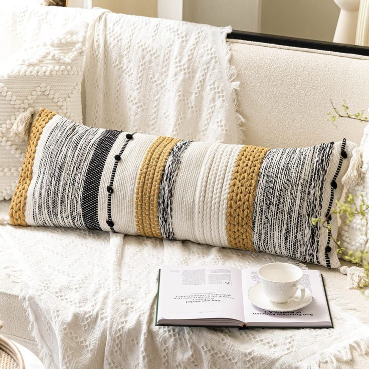 a white couch with a coffee cup and book on top of it next to a pillow