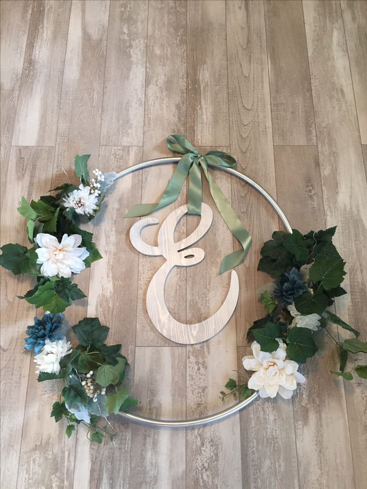 a wooden monogramm with flowers and greenery around it on a wood floor