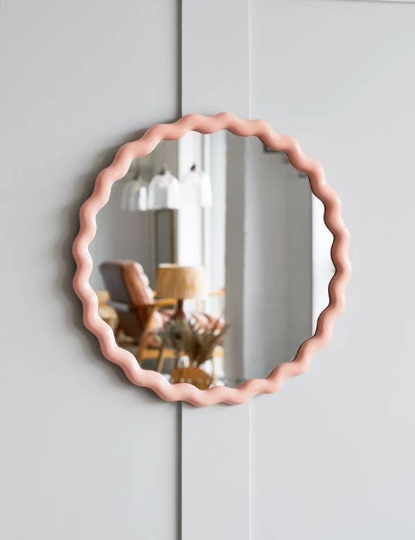 a round mirror hanging on the side of a white wall next to a chair and lamp