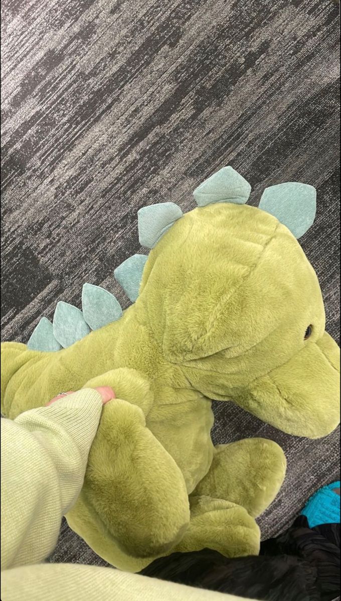 a green stuffed animal laying on top of a bed next to a person's leg