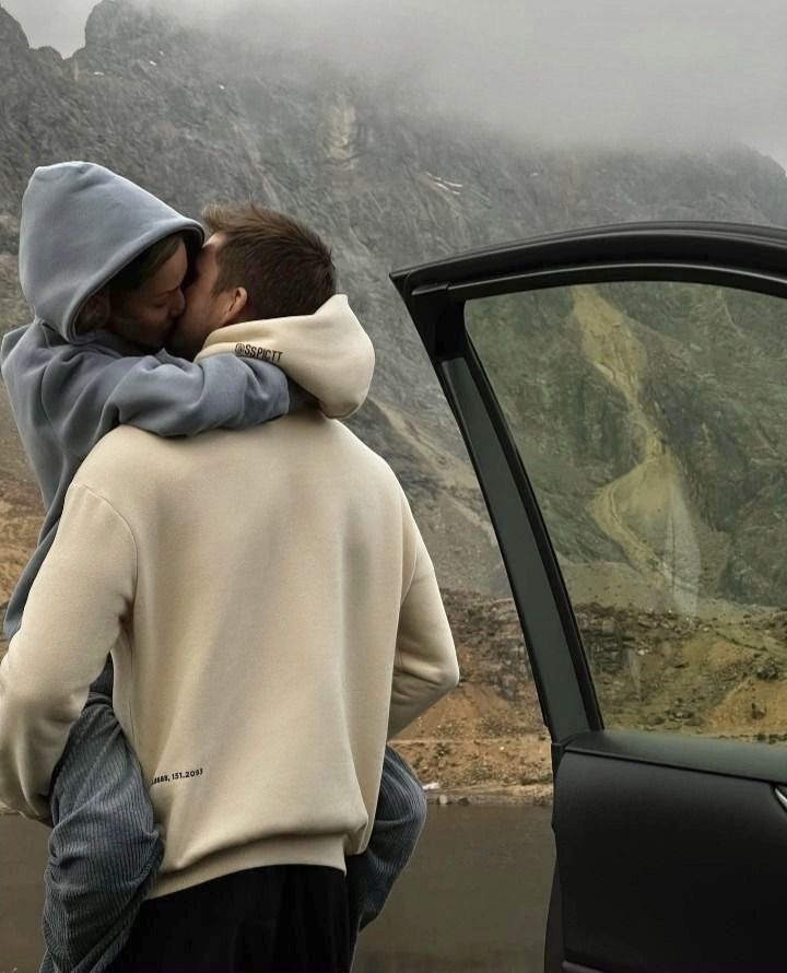 two people are standing in front of a car with the door open and one person is hugging another