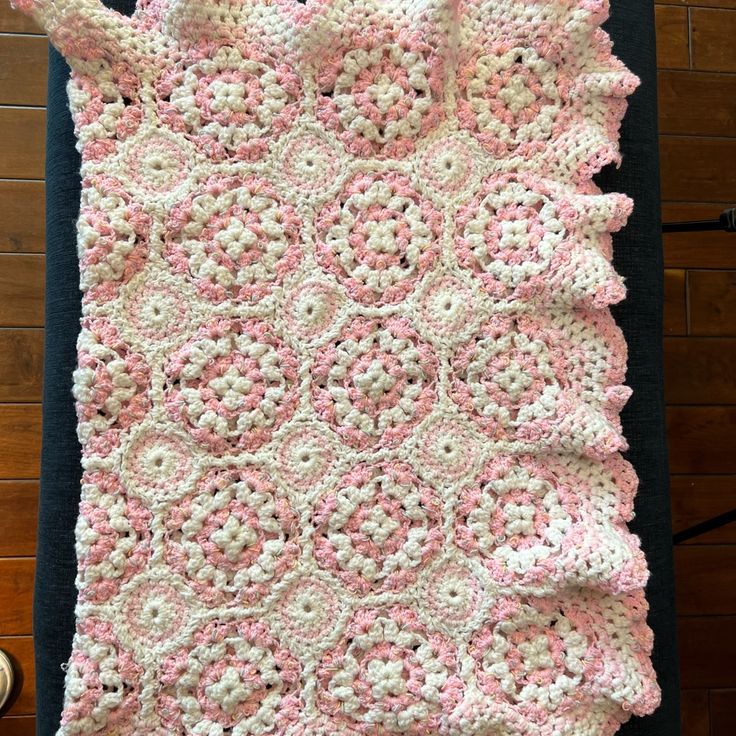 a pink and white crocheted blanket sitting on top of a black tablecloth