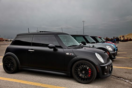 three cars parked in a parking lot with people standing around them and dark clouds overhead