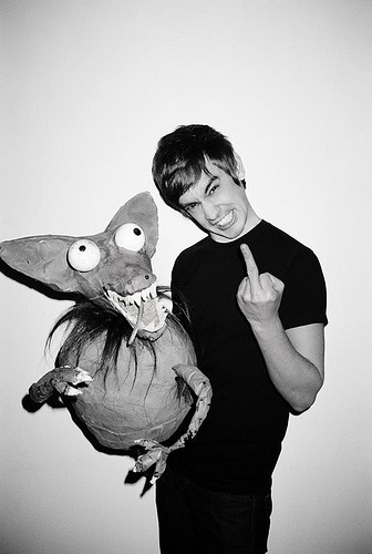 a young man holding a stuffed animal and giving the thumbs up sign while standing in front of a white wall