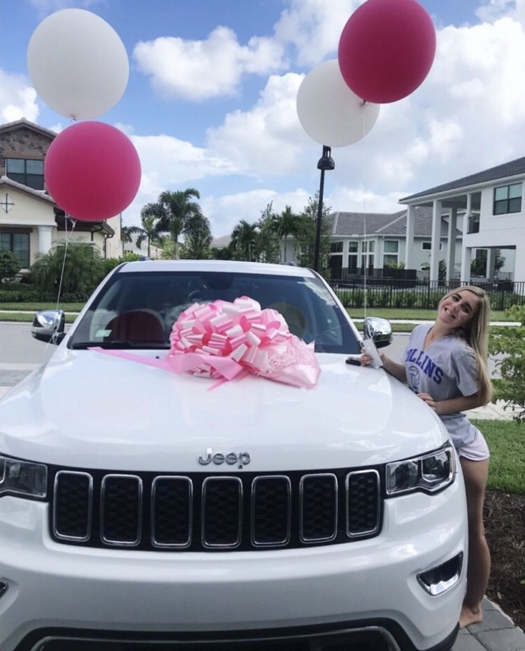 a woman standing next to a white jeep with pink and white balloons on the hood