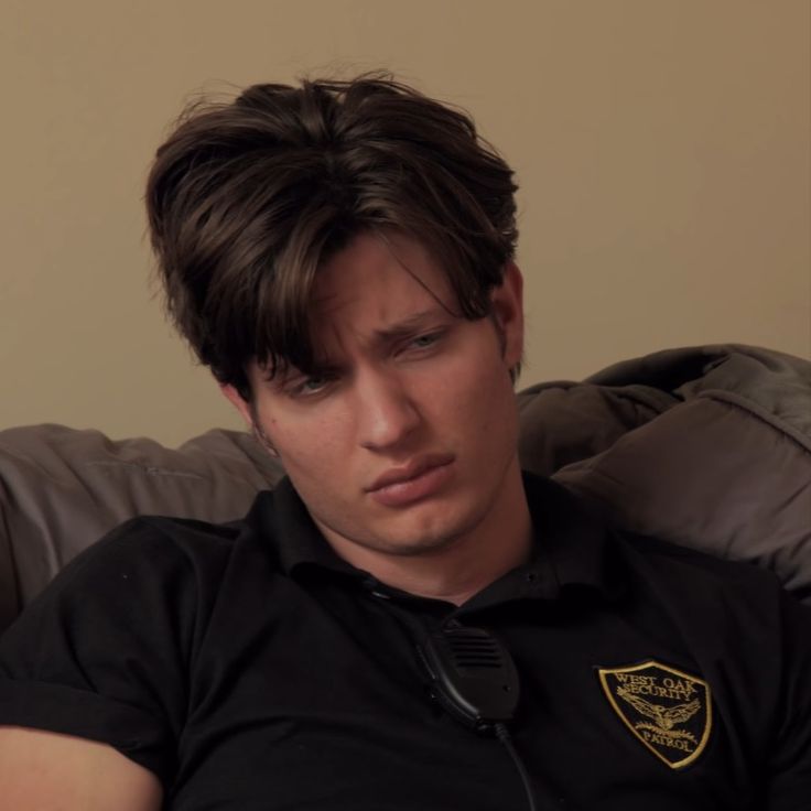 a young man sitting on top of a couch wearing a black shirt and gold badge