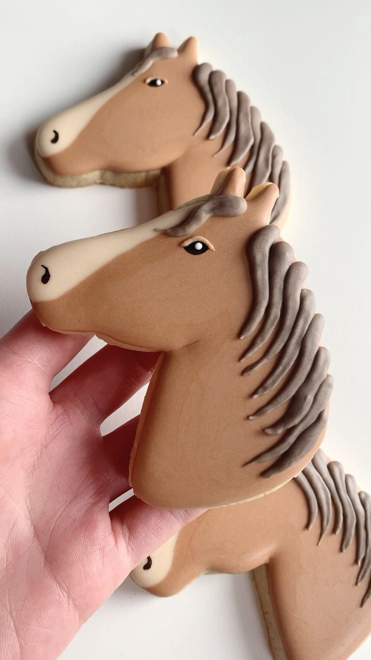 two cookies shaped like horses are being held by a person's hand on a white surface