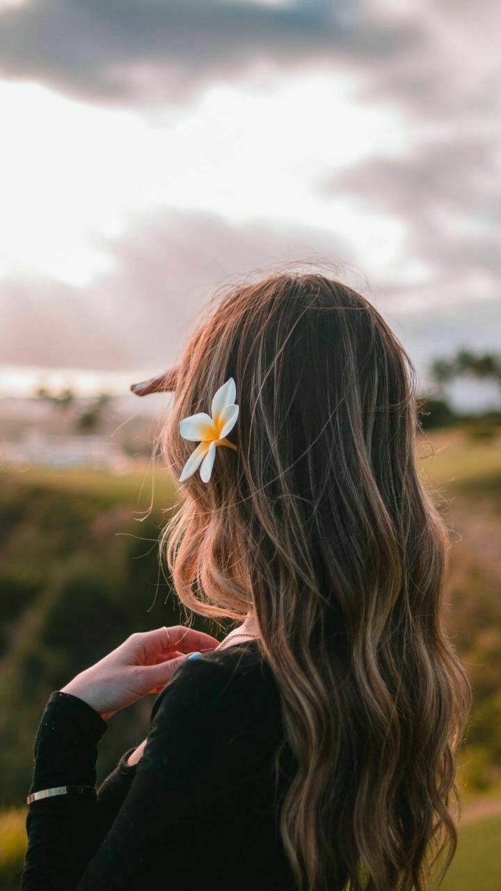 a woman with long hair and a flower in her hair is looking at the sky