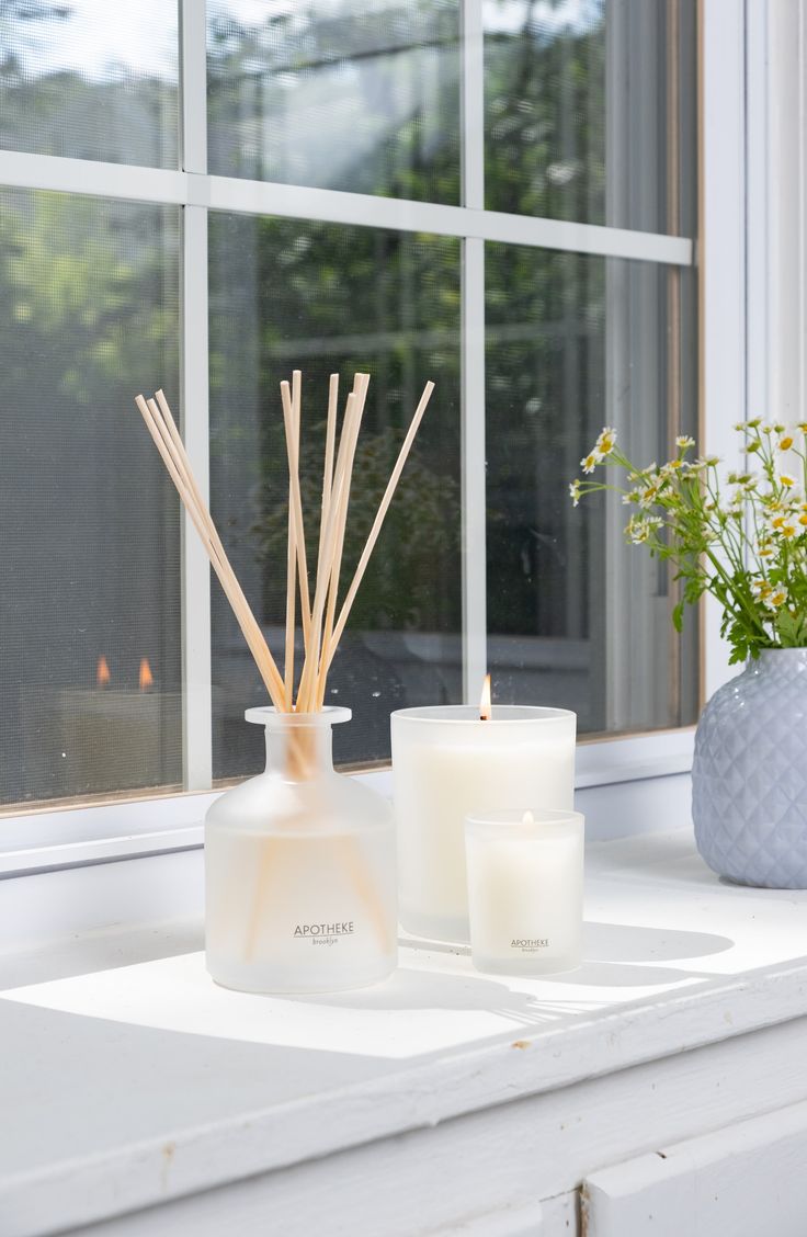 two candles sit on a window sill next to a vase with flowers