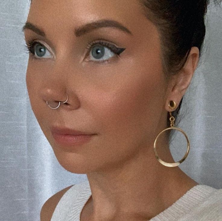 a woman with large hoop earrings and piercings on her nose looking at the camera