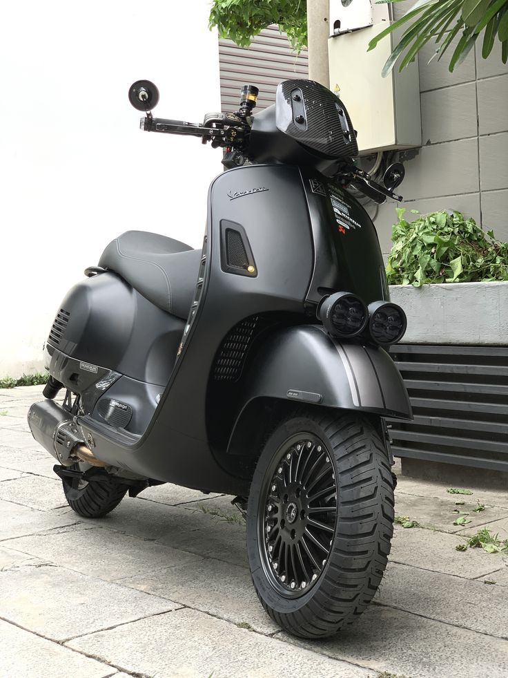 a motor scooter parked on the sidewalk next to a wall and planters