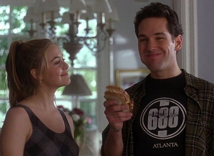 a man and woman standing in a living room eating food from each other's hands