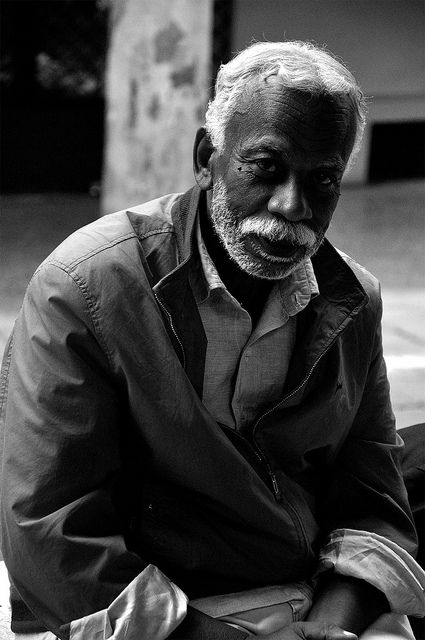 black and white photograph of an old man sitting on the ground