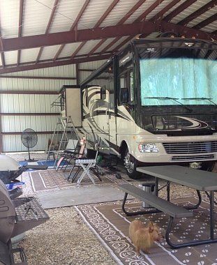 an rv parked in a garage with picnic tables and chairs around the camper area