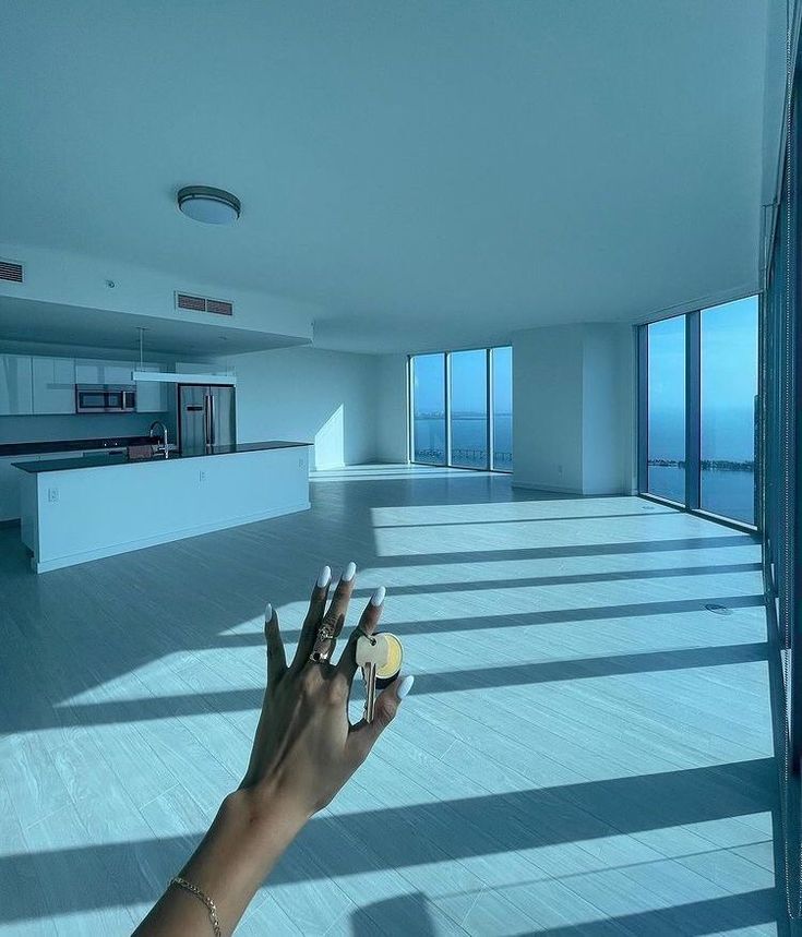 a person's hand reaching out towards an empty room with large windows and floor to ceiling windows