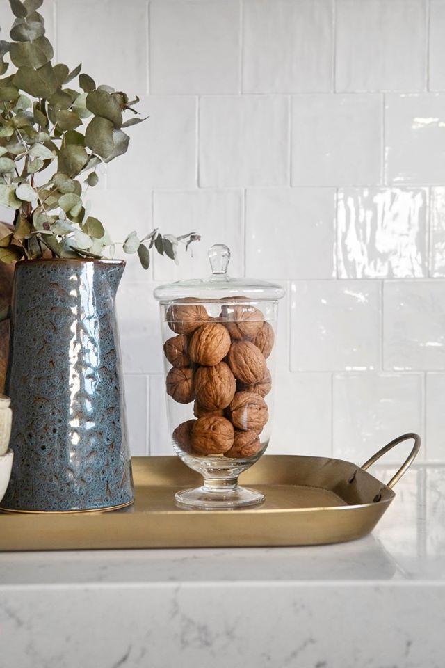 some nuts are in a glass bowl on a tray next to a potted plant