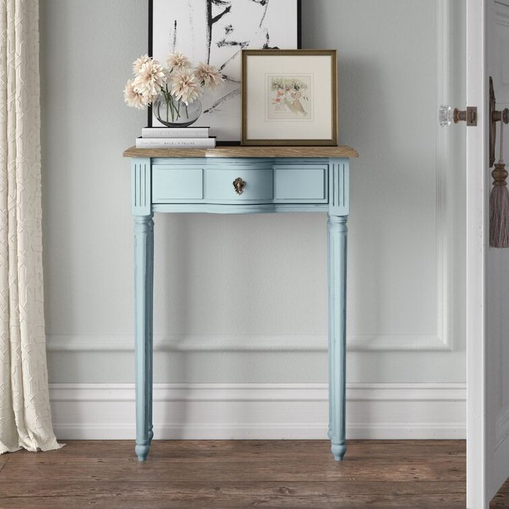 a small white table with flowers on it in front of a door and framed pictures