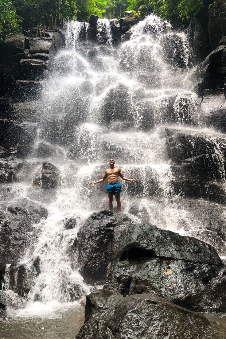 a man standing in front of a waterfall with his arms spread out and hands behind him