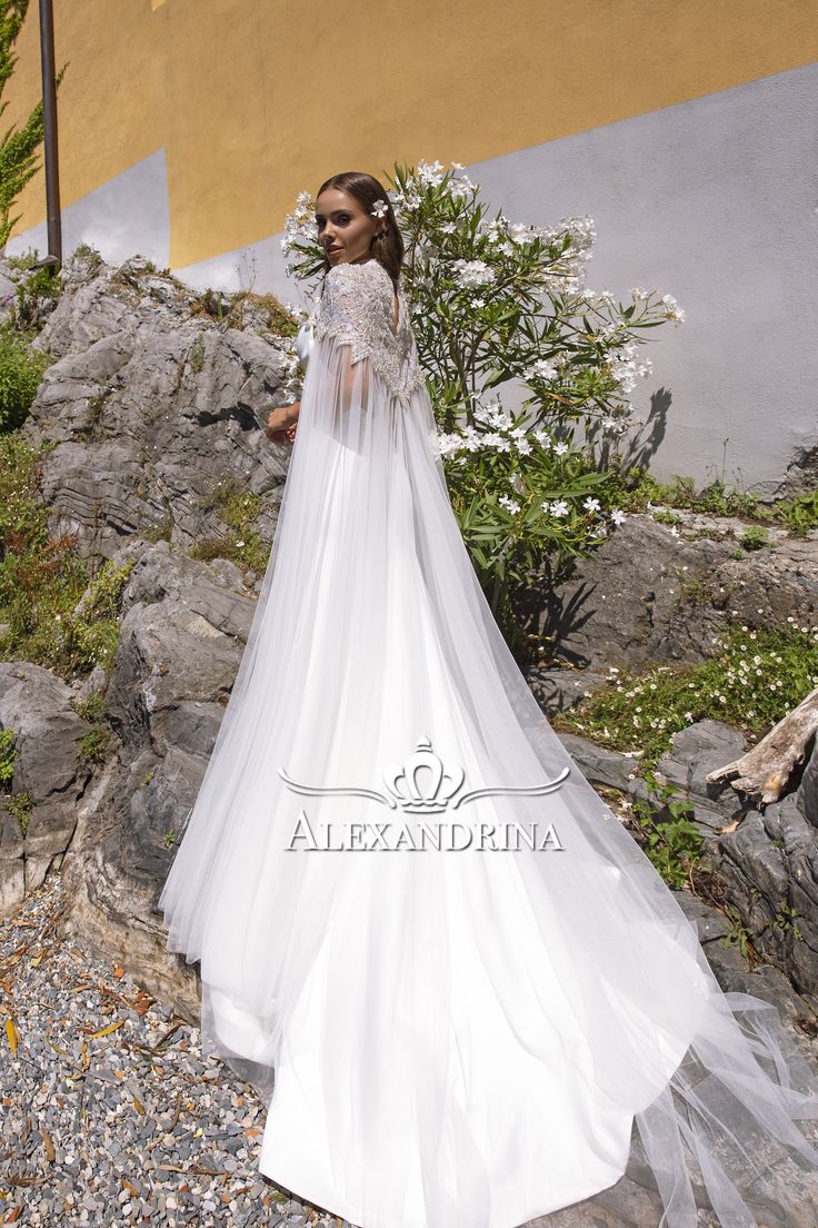 a woman in a white wedding dress standing on rocks with flowers behind her, looking at the camera