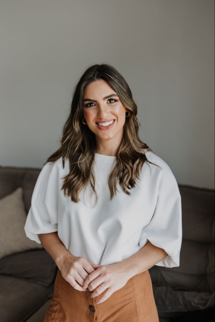 a woman standing in front of a couch with her hands on her hips and smiling