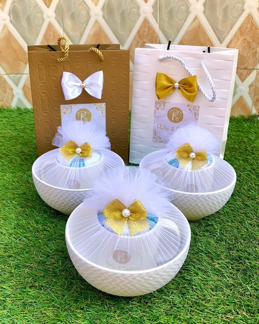 three white bowls with yellow bows on them sitting in the grass next to a brown bag