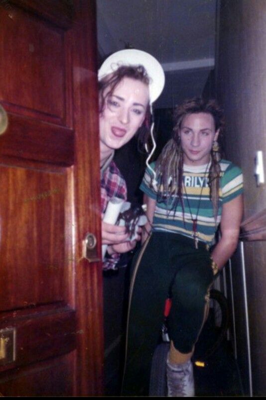 two young women standing next to each other in front of a wooden door and looking at the camera