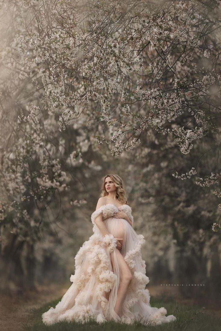 a pregnant woman in a dress standing under a tree with white flowers on it's branches