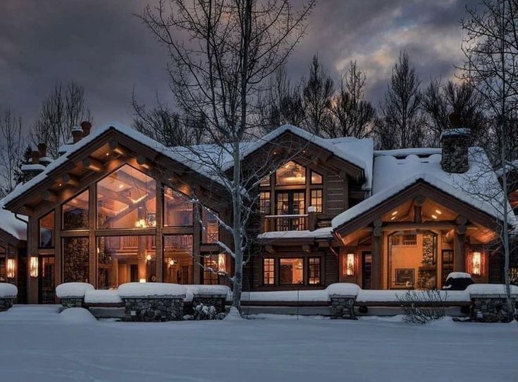 a large house with lots of windows and lights on in the snow covered yard area