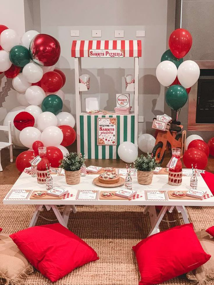 a table set up for a party with red, white and green balloons in the background