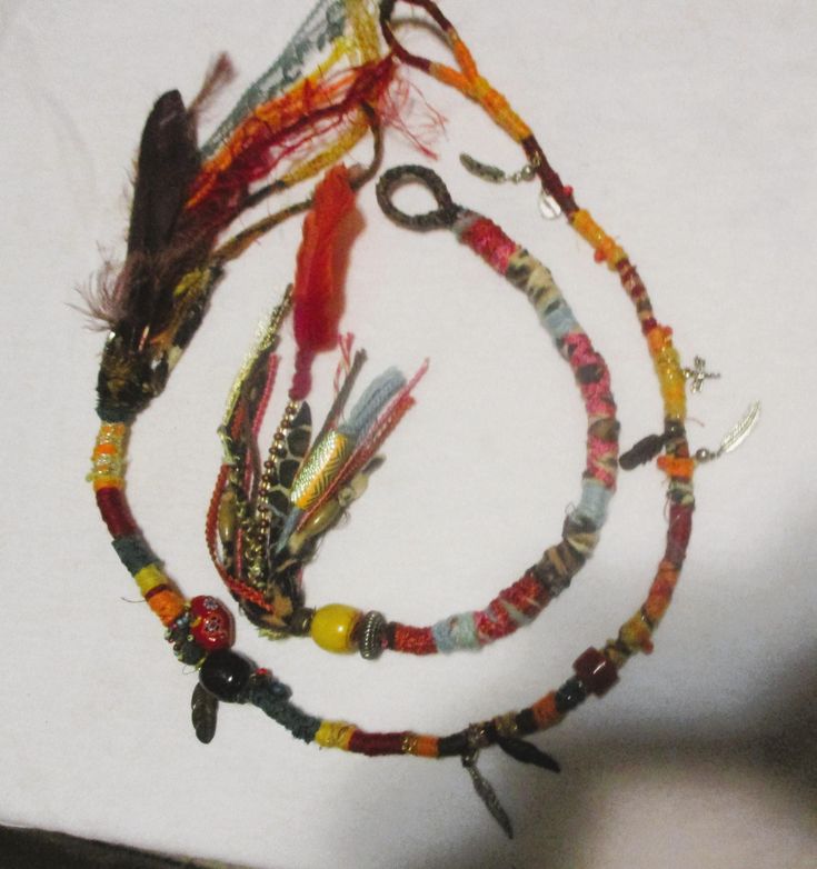 several bracelets with feathers and beads are on a white surface, while someone is holding one in the other's hand