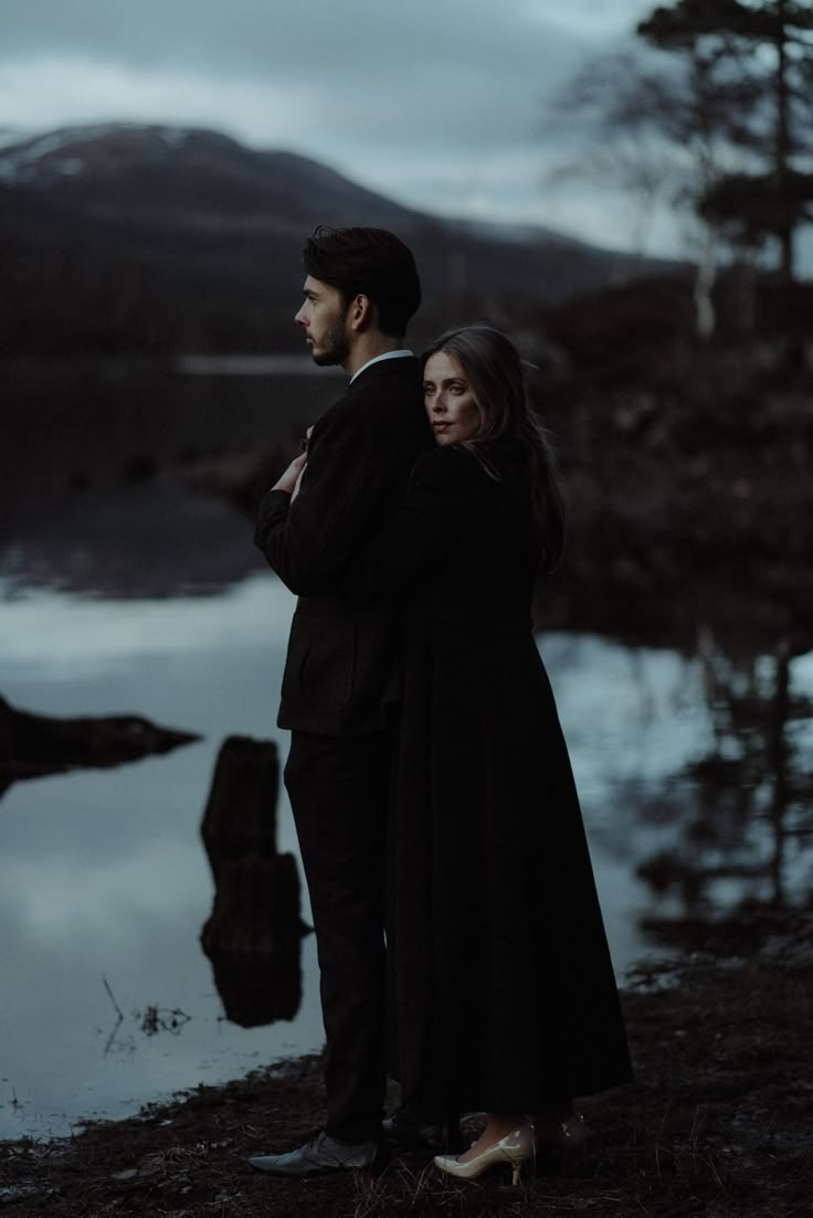 a man and woman standing next to each other in front of a body of water