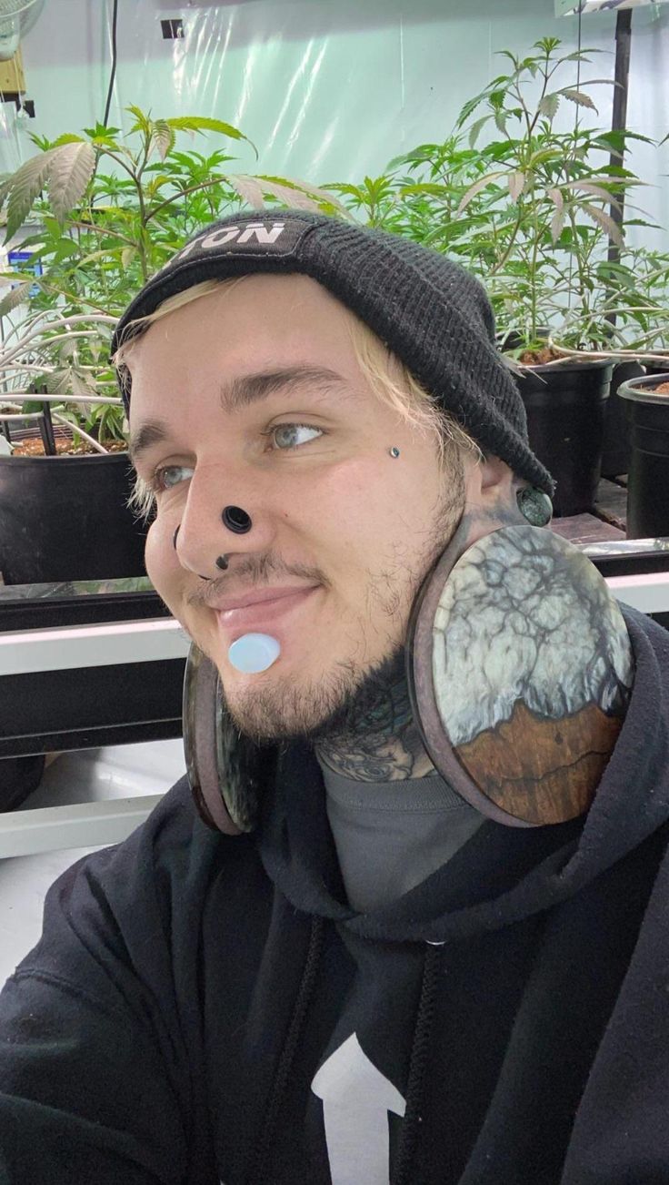 a man with tattoos and piercings on his ears is sitting in front of potted plants