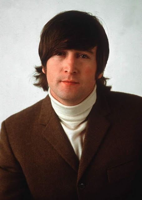 a man with long hair wearing a brown suit and white turtle neck sweater is looking at the camera