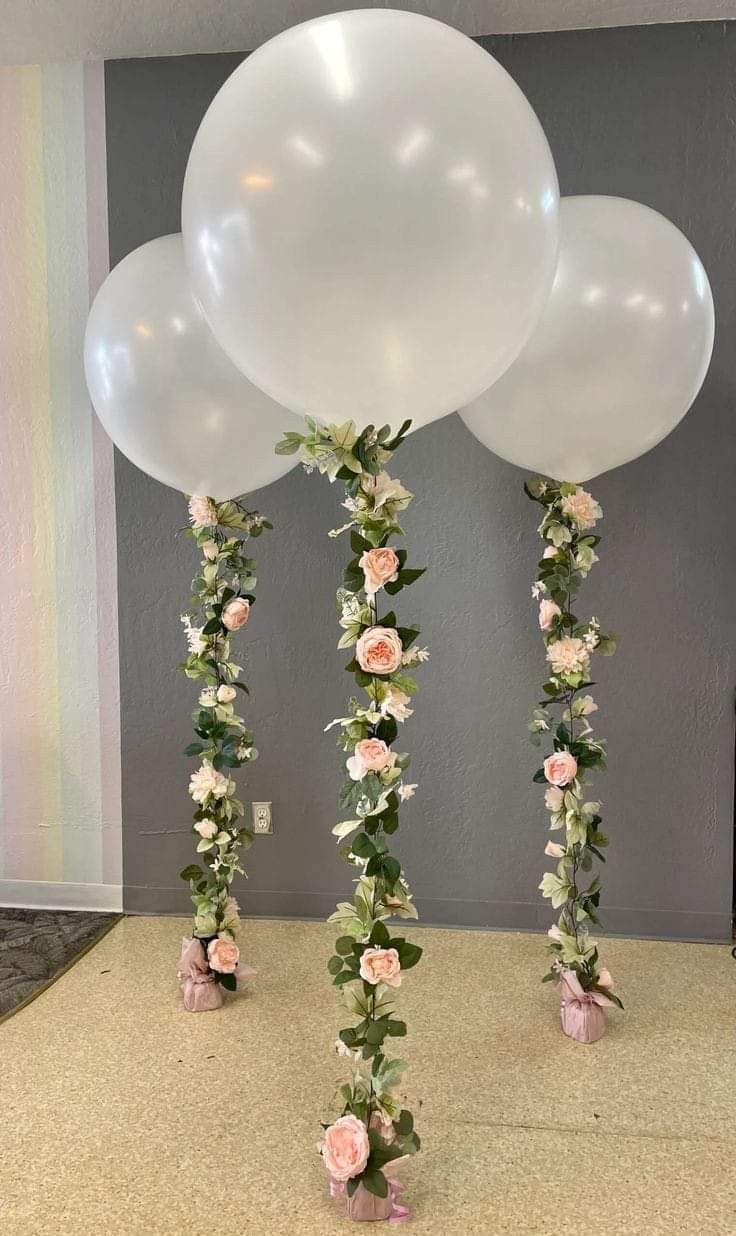 three large white balloons with flowers and greenery on the bottom are standing in front of a gray wall