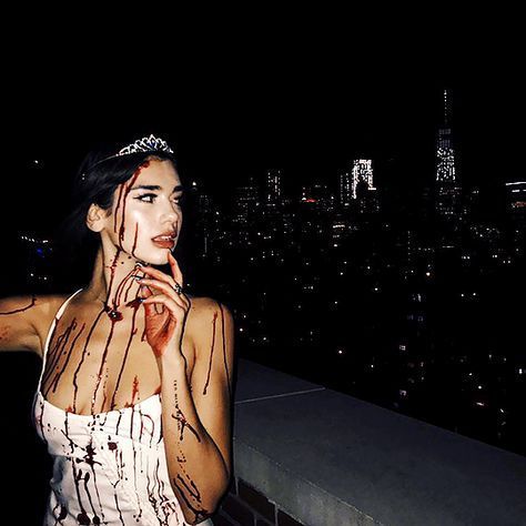 a woman with blood all over her body standing on top of a building at night