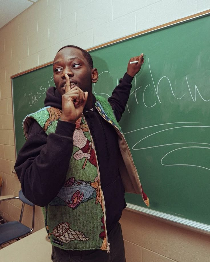 a man standing in front of a blackboard with writing on it and pointing to the side