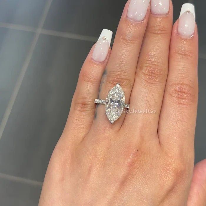 a woman's hand with a diamond ring on top of her finger and white nails