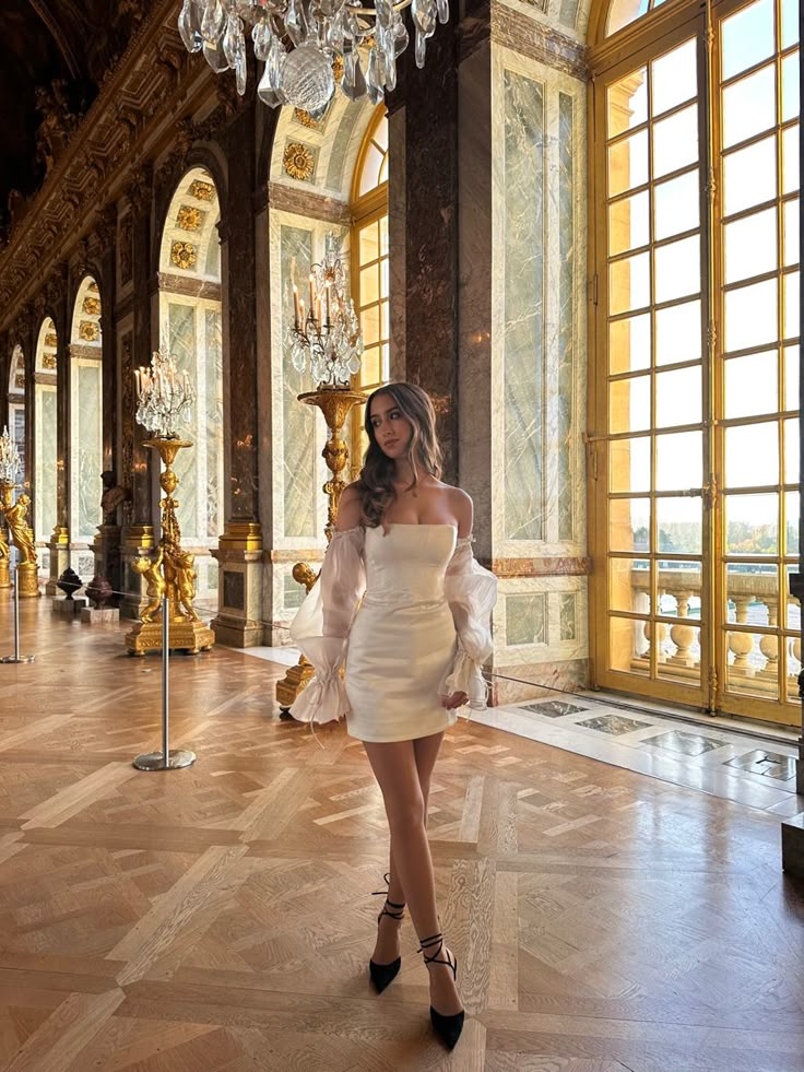 a woman in a white dress posing for the camera with chandelier hanging from the ceiling